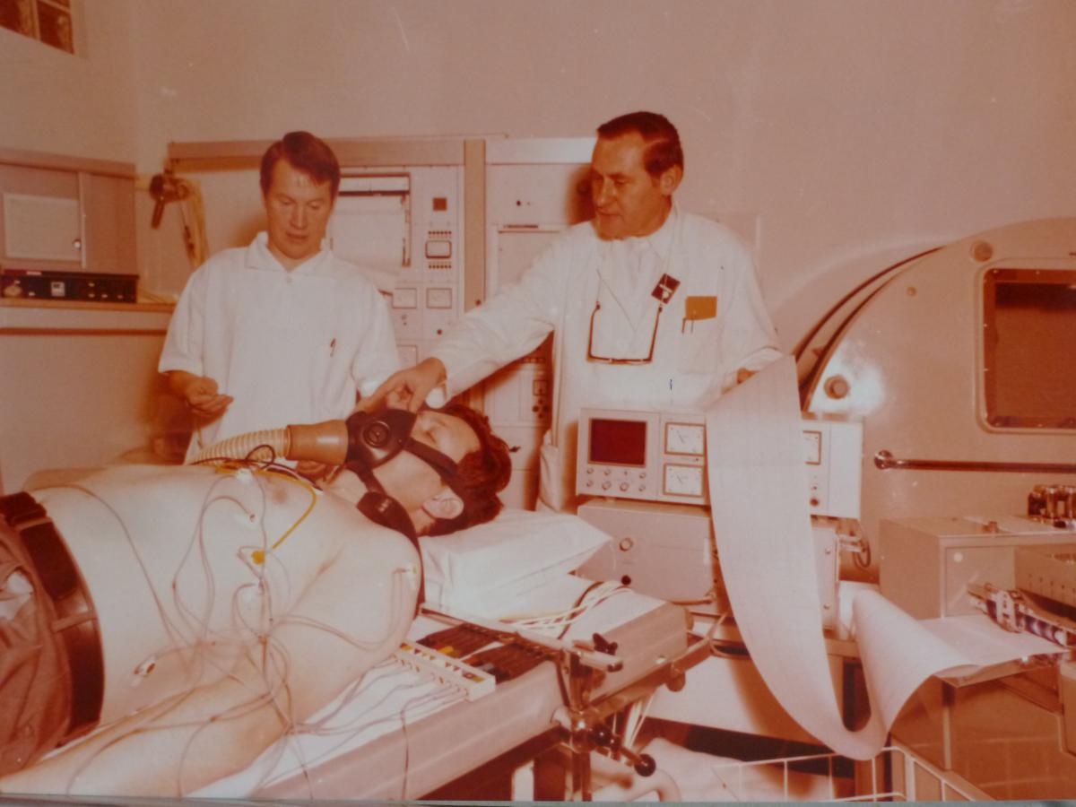 Patient auf Liege mit Atemmaske, dabei ein Pfleger und der damalige Auguste-Chefarzt Dr. med. Harald Gonschewski im Jahr 1977